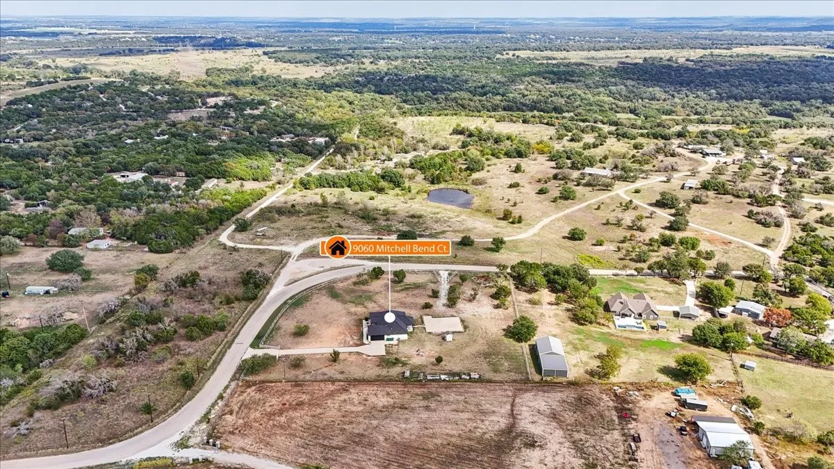 Aerial perspective of a sprawling property featuring expansive acreage, a metal-roofed residence, a detached secondary structure, and established tree clusters