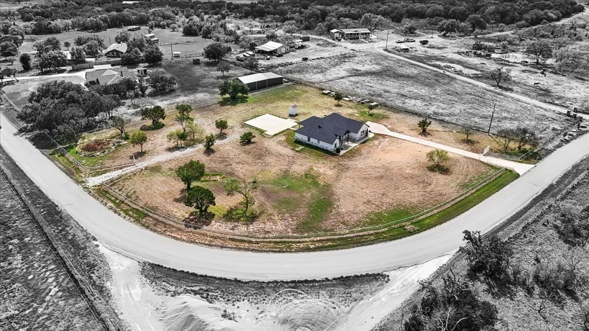 Aerial perspective of a corner lot featuring an expansive yard, concrete driveway, detached storage structure, and mature trees