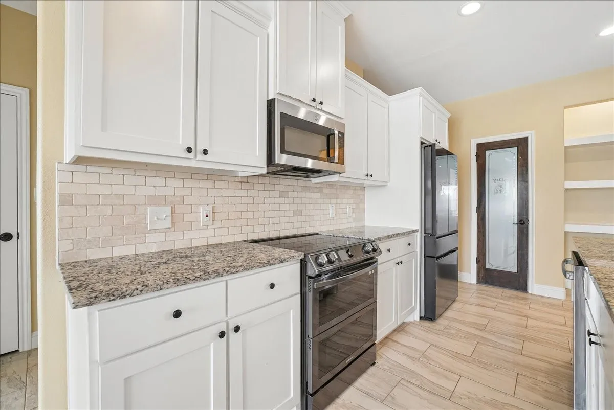 White shaker-style cabinetry, stone-finish countertops, subway tile backsplash, stainless steel appliances, and wood-finish tile flooring