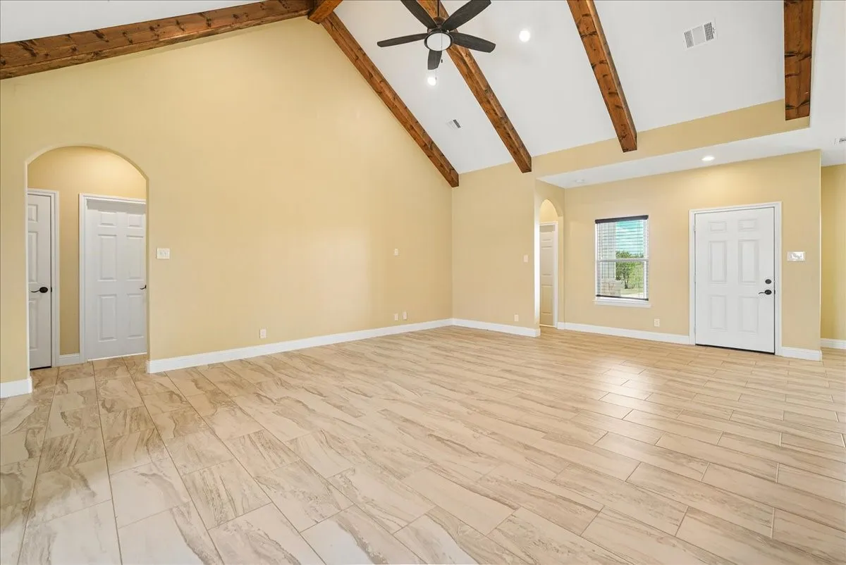 Vaulted ceiling with exposed wood beams, neutral-tone tile flooring, arched doorways, and recessed lighting