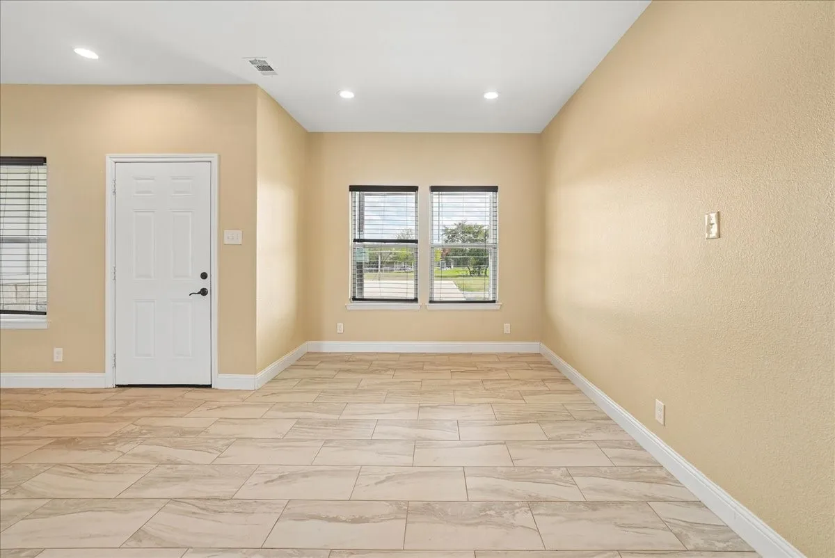 Neutral-toned interior space featuring light-colored stone-finish floor tile, recessed ceiling lighting, and dual windows