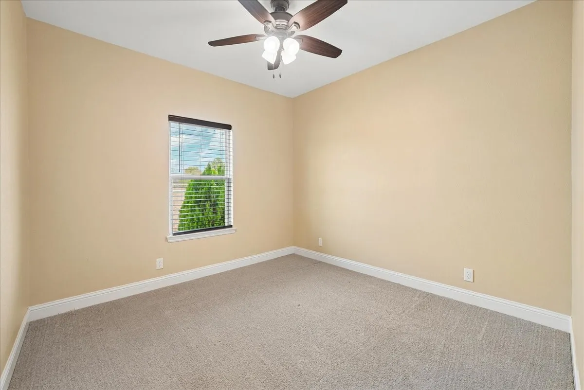 Neutral interior room featuring neutral wall paint, carpeted flooring, a ceiling fan with integrated lighting, and a window with fitted blinds