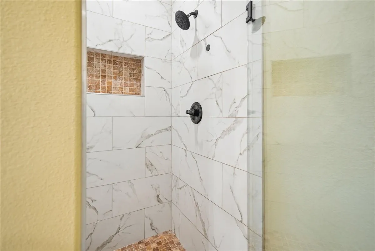 Walk-in shower featuring large-format veined wall tile, mosaic tile floor and recessed niche, matte black fixtures, and a glass door