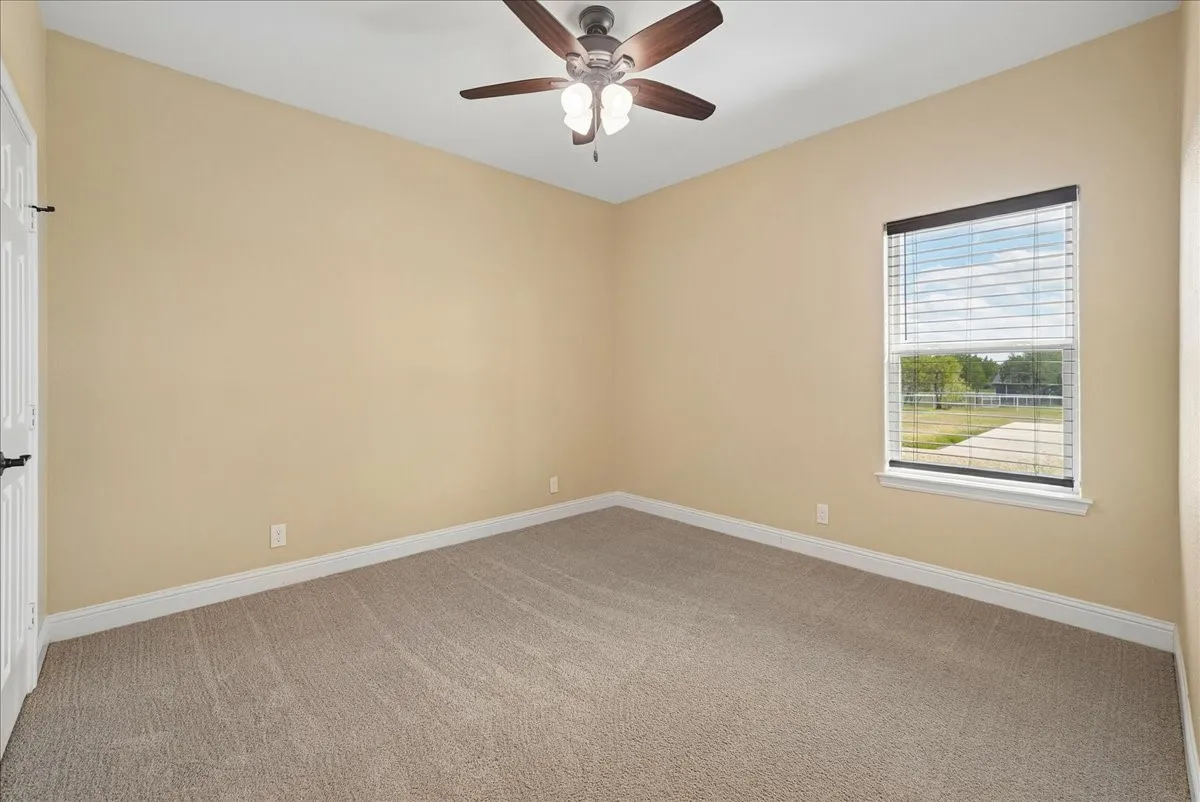 Room featuring neutral wall tones, wall-to-wall carpeting, a multi-blade ceiling fan with integrated lighting, and a window with horizontal blinds