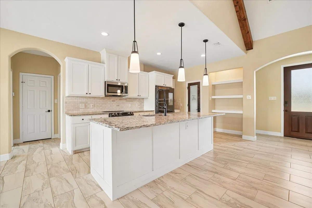 Kitchen featuring white cabinetry, an expansive central island with stone-finish countertops, tile backsplash, pendant lighting, and wood-finish flooring