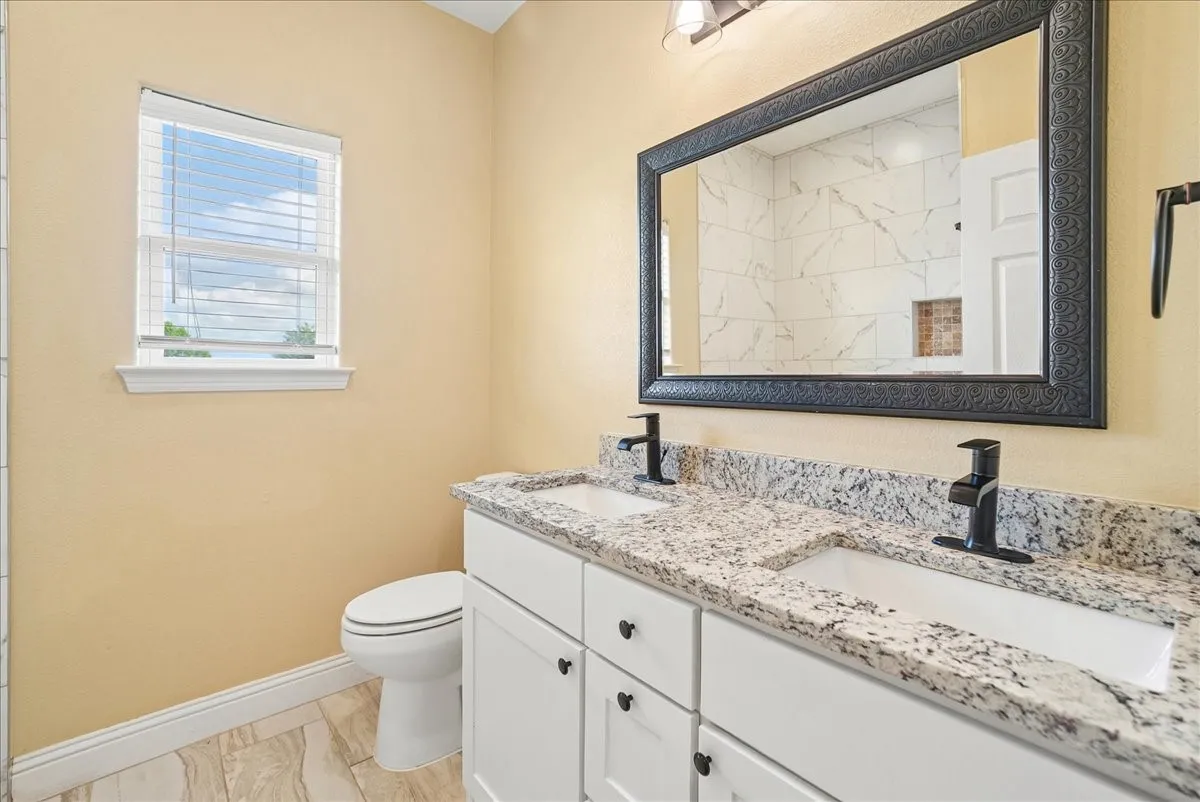 Double vanity featuring stone countertops, dual under-mount sinks, matte black faucets, white shaker-style cabinetry, and a framed mirror