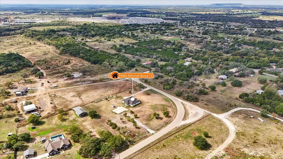 Aerial view of a sprawling property featuring a paved driveway, detached secondary structure, and extensive open acreage