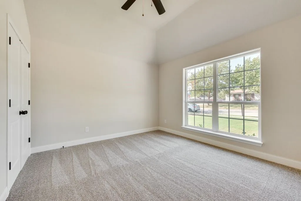 Vaulted ceilings, neutral carpeting, expansive multi-pane window, and a ceiling fan