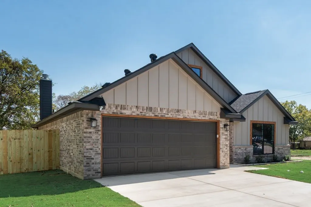 Exterior featuring a combination of brick and vertical panel siding, a shingle roof, a two-car garage, and an integrated masonry chimney