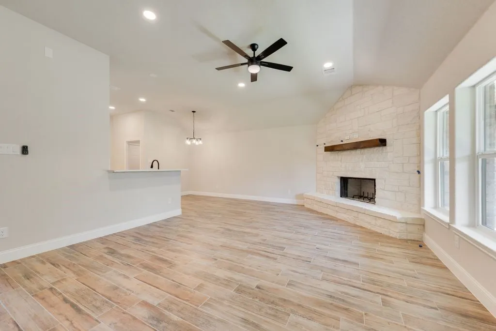 Vaulted ceiling featuring a stone-clad fireplace with a timber mantel, wood-finish flooring, recessed lighting, and a breakfast bar