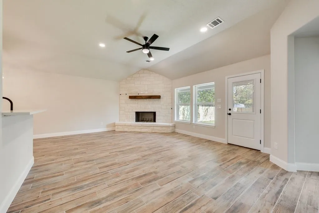 Vaulted ceiling, stone-accented fireplace with a wood mantel, wood-finish flooring, recessed lighting, and a ceiling fan