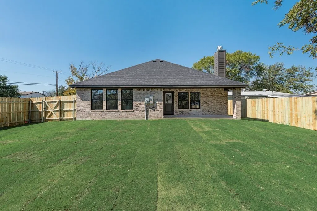 Brick exterior, asphalt shingle roof, chimney stack, rear covered patio, and fenced-in lawn