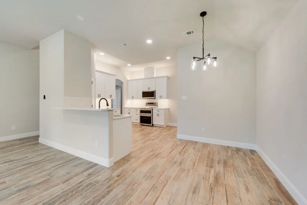 Kitchen featuring white cabinetry, wood-finish flooring, stainless steel appliances, a peninsula with an integrated sink, and an overhead chandelier