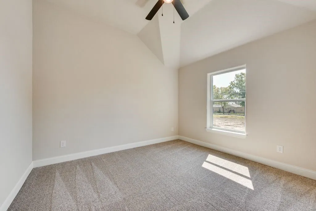 Vaulted ceiling featuring a ceiling fan with integrated lighting, neutral wall paint, and wall-to-wall carpeting