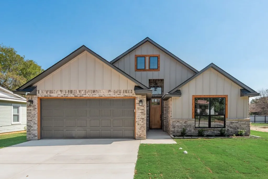 Exterior featuring board-and-batten siding, stone masonry accents, a wood-trimmed entry door, a multi-car garage, and dark-framed windows