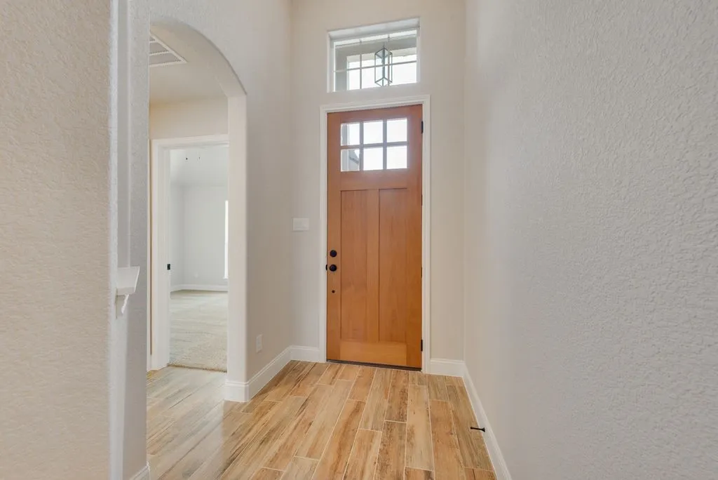 Entryway featuring wood-finish tile flooring, arched passageway, wood-frame door with glass inserts, and transom window