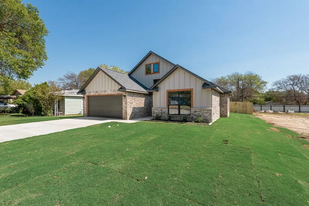 Exterior featuring vertical board-and-batten siding, multi-gabled roofline, brick masonry, concrete driveway, and attached two-car garage