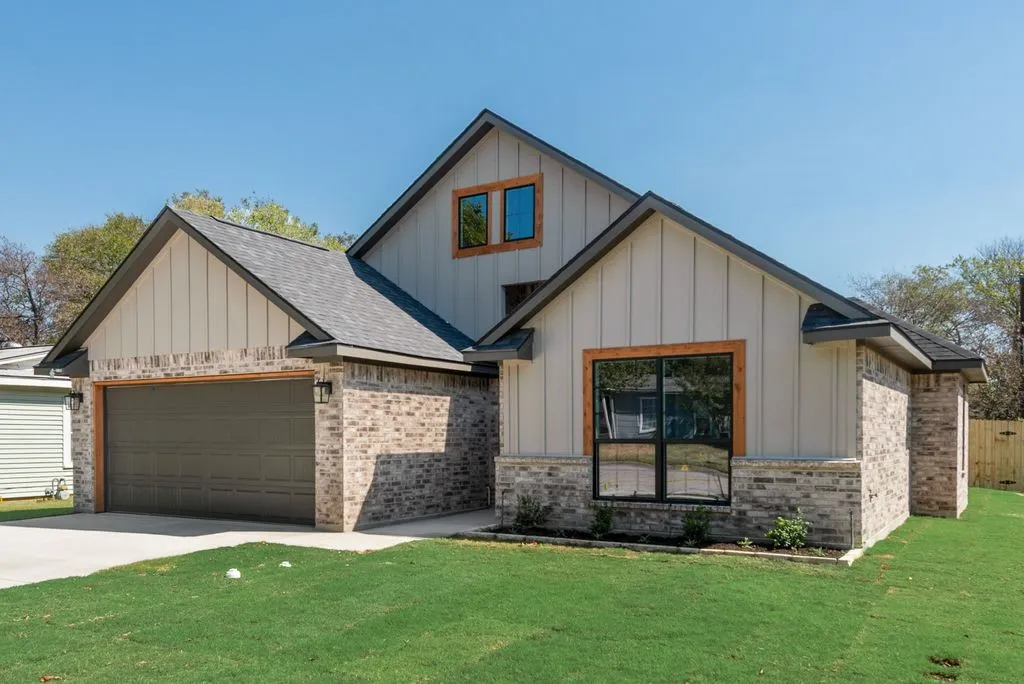 Exterior facade featuring vertical board-and-batten siding, mixed-media brick masonry, a multi-gabled roofline, wood-trimmed window frames, and a two-car garage