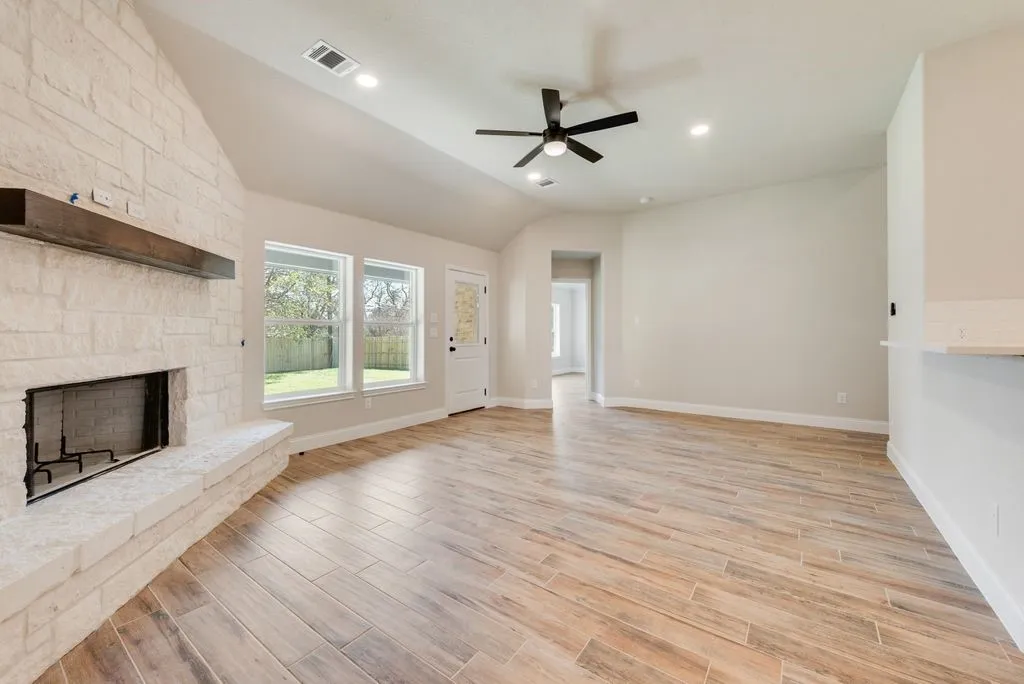 Vaulted ceiling featuring a floor-to-ceiling stone fireplace, wood-finish tile flooring, recessed lighting, and a modern ceiling fan