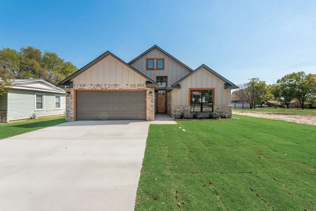 Exterior facade featuring vertical siding and stone veneer, multi-gabled roofline, concrete driveway, and covered entryway