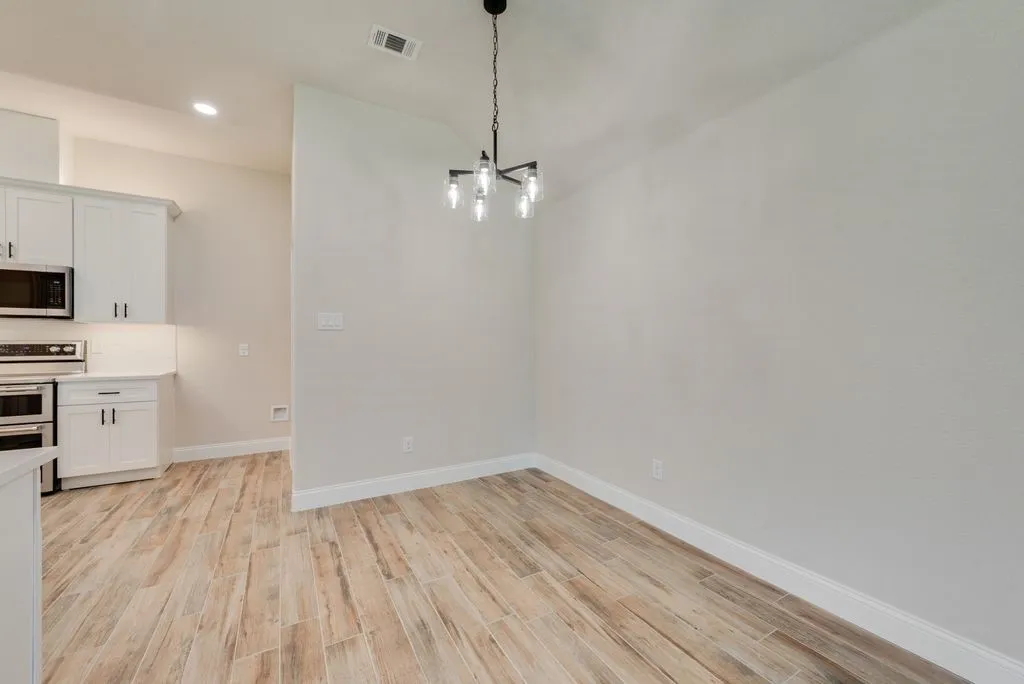 Wood-finish flooring, multi-light geometric chandelier, and white cabinetry featuring contrasting hardware