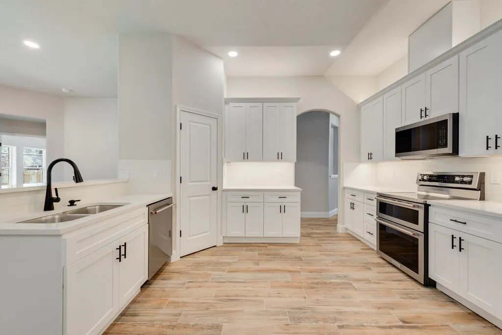 Kitchen featuring white cabinetry, wood-finish flooring, stainless steel appliances, matte black hardware, and recessed lighting