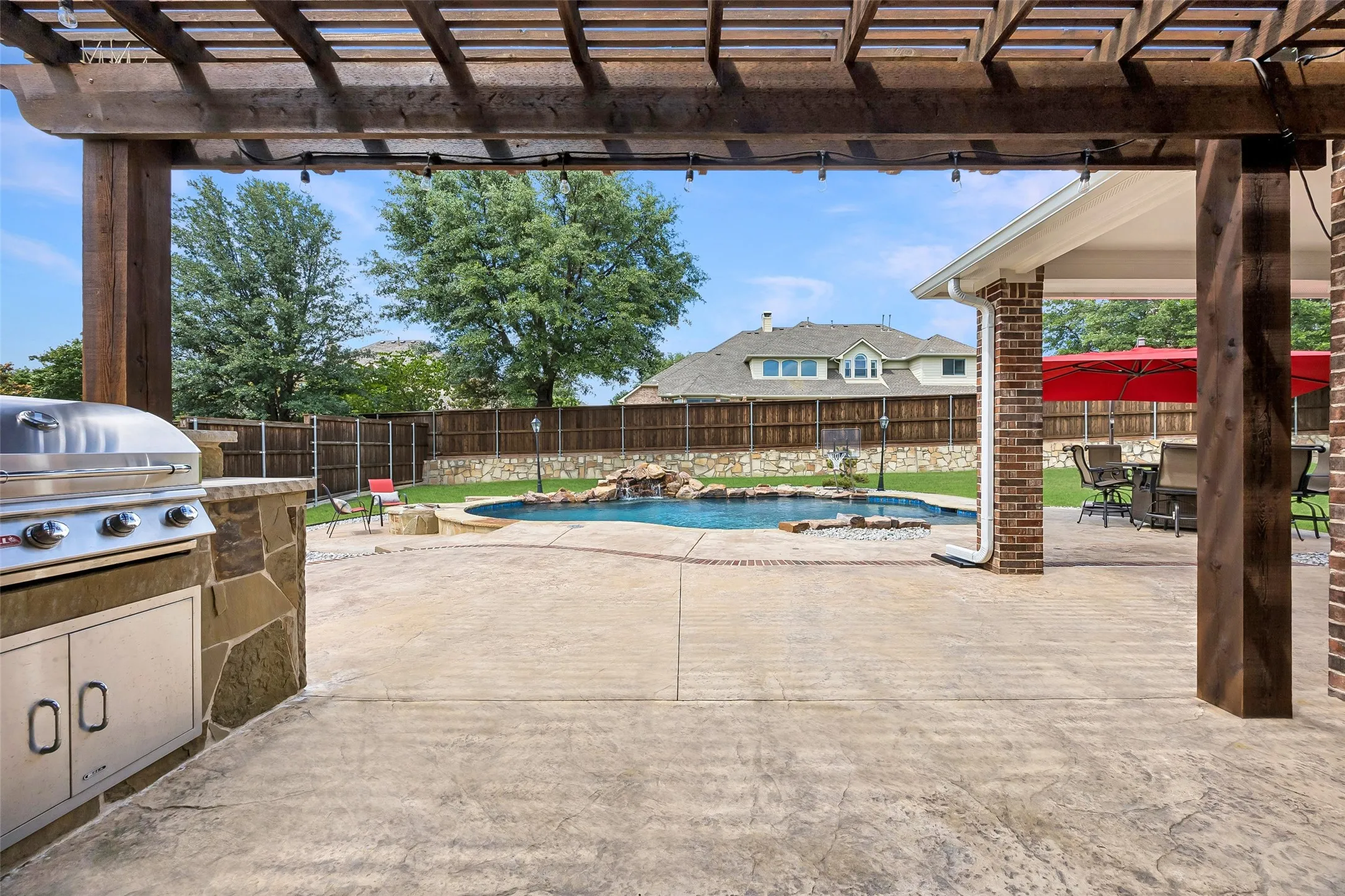 Resort-style backyard featuring a sparkling pool,pergola-covered patio with built-in grill, and multiple spaces for outdoor entertaining.