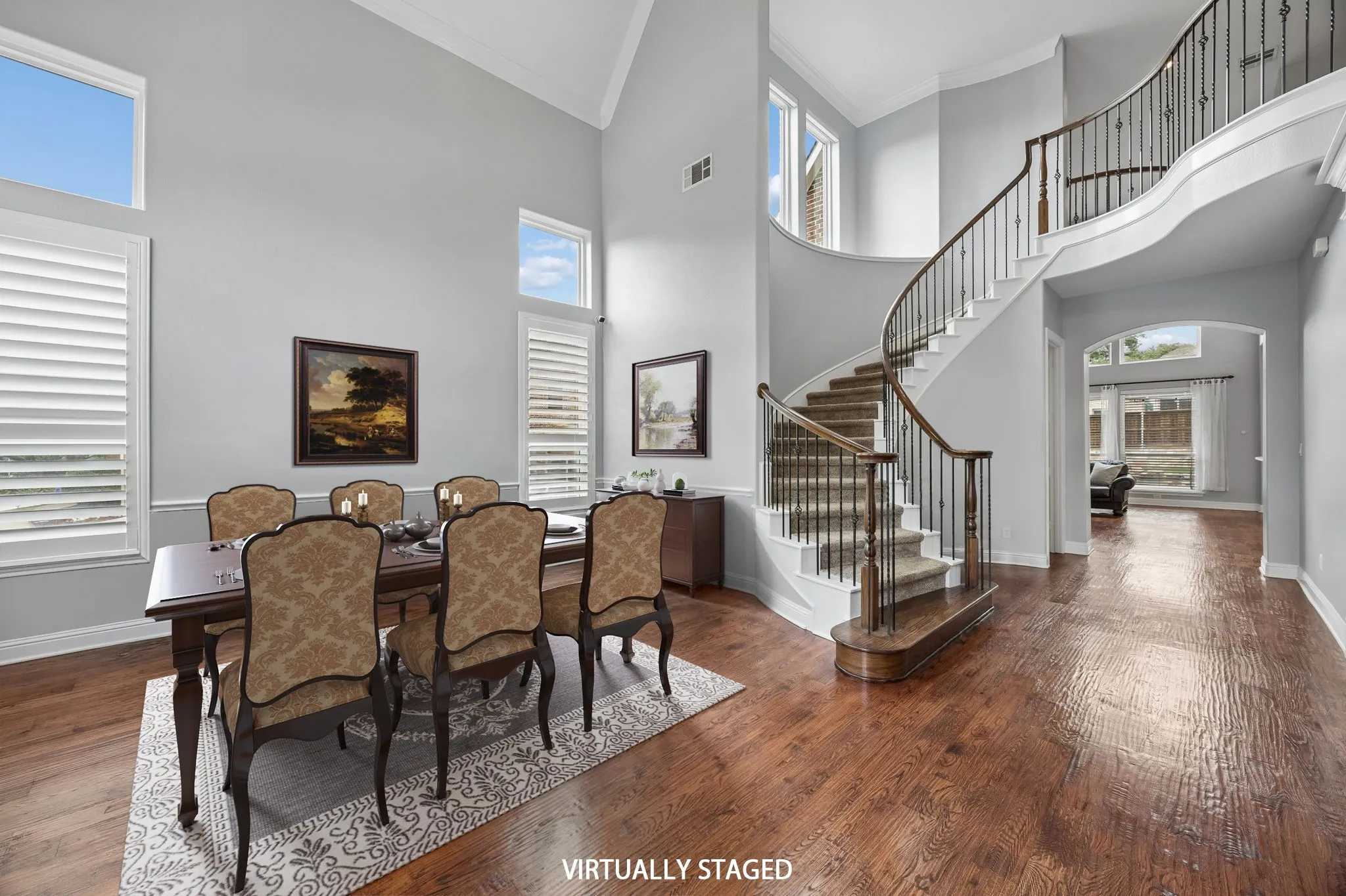 Dining area with soaring ceilings, rich wood floors,and a sweeping staircase that creates a stunning first impression.