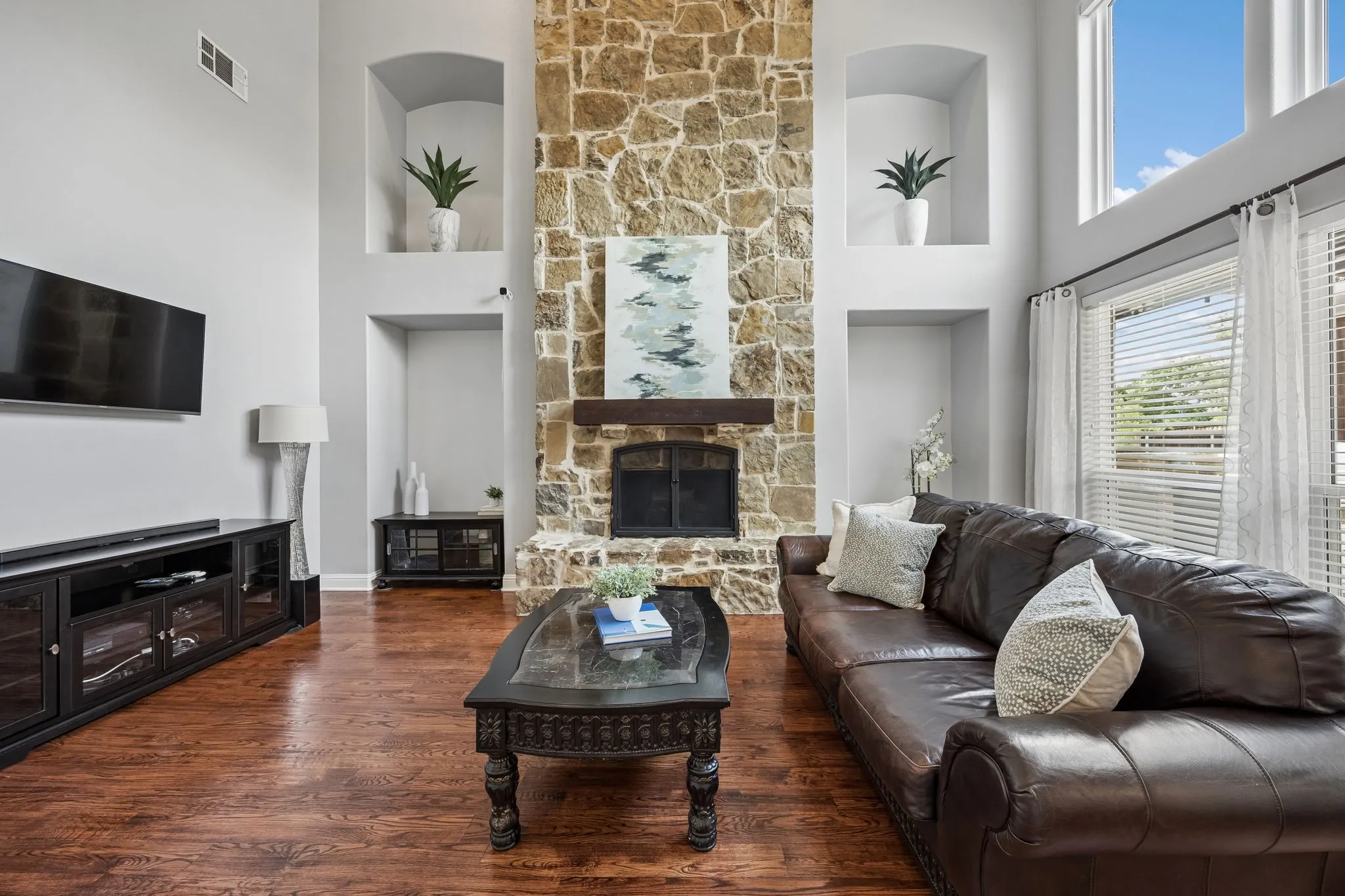 Soaring ceilings and a dramatic floor-to-ceiling
stone fireplace create a stunning focal point in this light-filled living room, complete with rich wood floors and oversized windows.