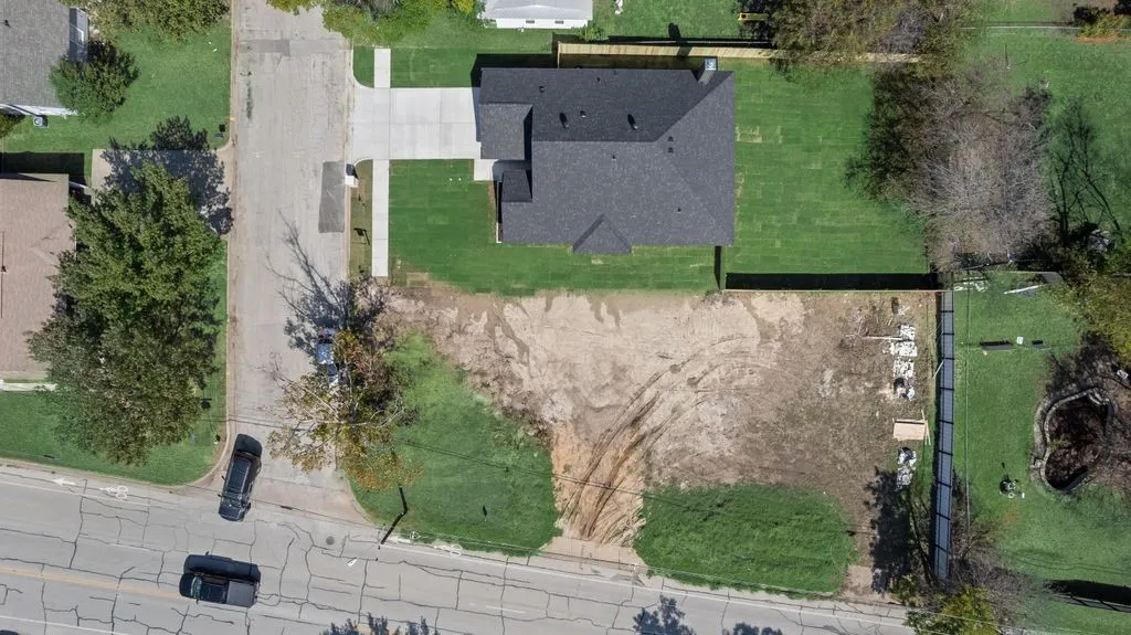 Aerial perspective of a property featuring a corner lot, concrete driveway, and peripheral wood fencing