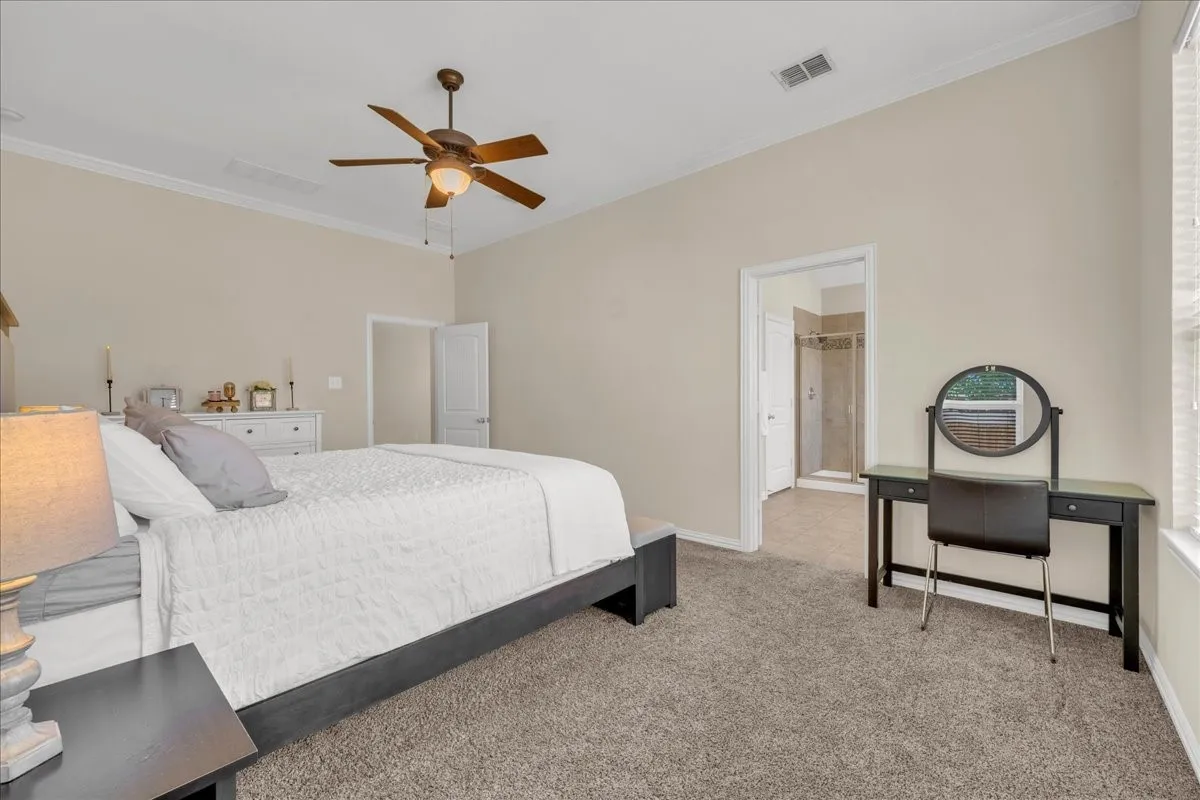 Vaulted ceiling with crown molding, ceiling fan, carpet flooring, and an en-suite bathroom with a glass-enclosed shower