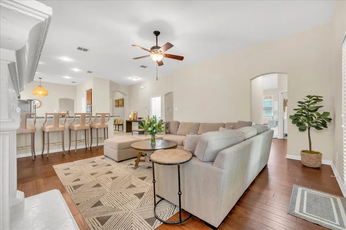 Hardwood-finish flooring, recessed lighting, and a ceiling fan are featured in this open-concept room with arched doorways