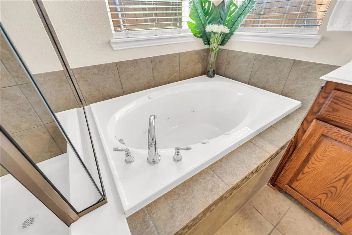 Corner soaking tub with polished chrome fixtures, tile surround, and adjacent glass-enclosed shower