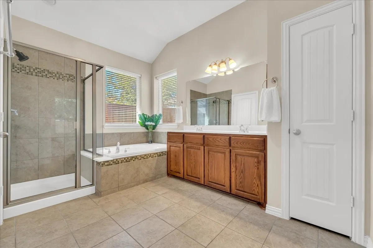 Spacious bathroom featuring a glass-enclosed shower, a separate soaking tub, dual vanity with wood cabinetry, and tiled flooring
