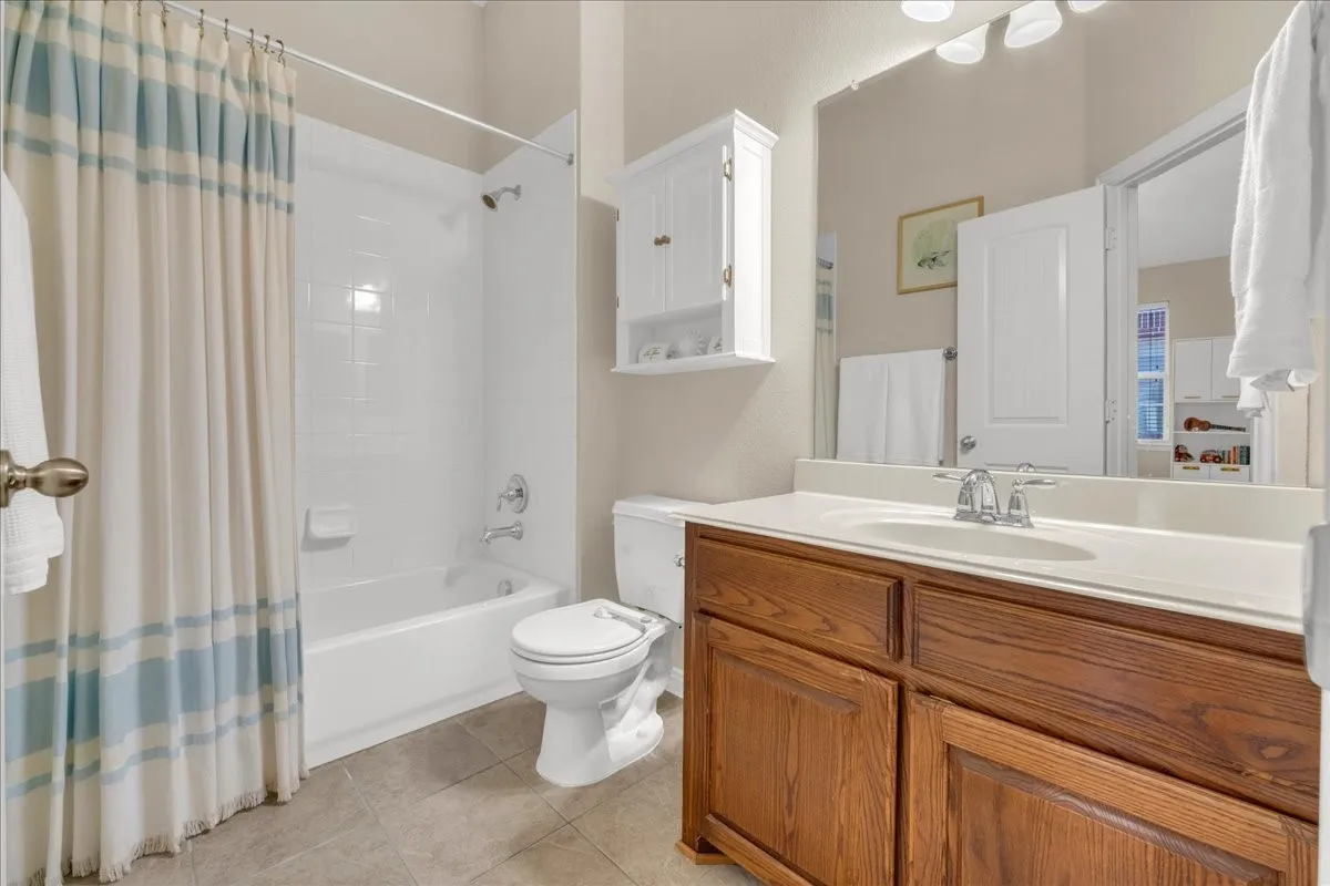 Bathroom featuring a built-in tub with shower, wood-finish vanity with a single basin sink, and a wall-mounted storage cabinet