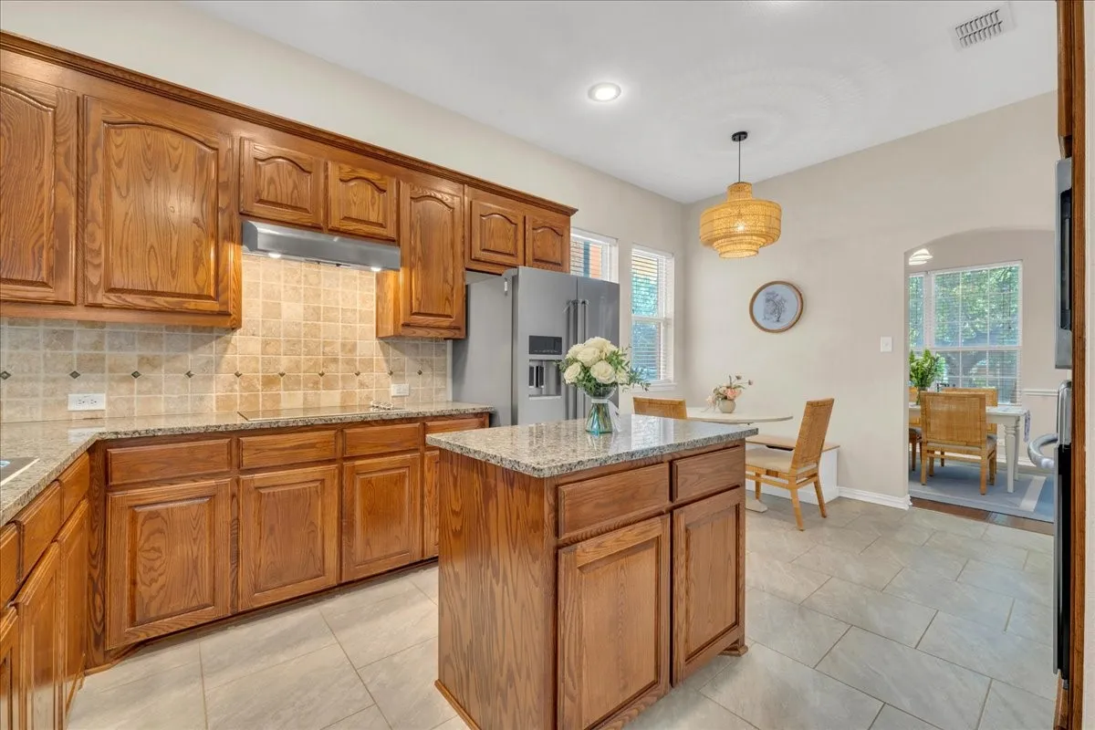 Kitchen featuring wood cabinetry, granite countertops, tile backsplash, and tile flooring