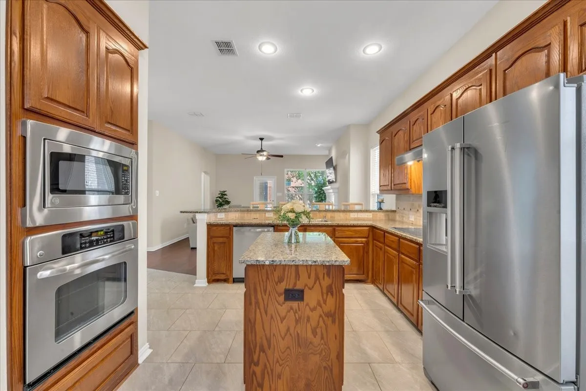 Kitchen featuring wood cabinetry, stainless steel appliances, a center island with a stone countertop, and tile flooring
