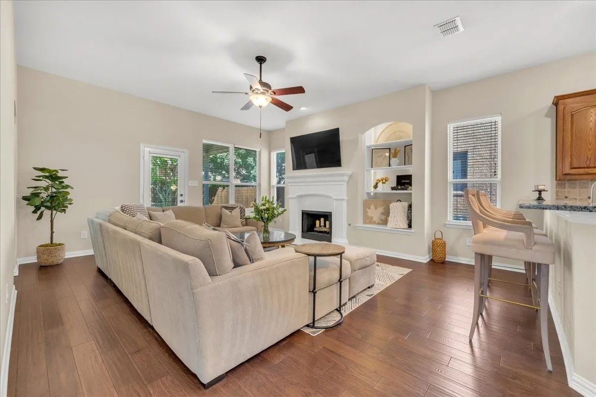 Wood-finish flooring throughout, vaulted ceiling with a ceiling fan, fireplace with a mantel, built-in shelving, and a breakfast bar with stone countertops