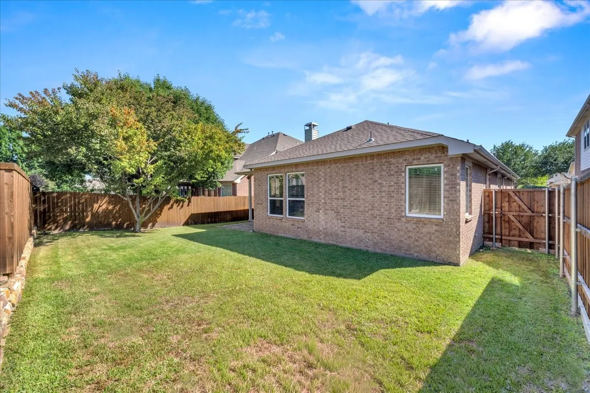 Brick exterior with a shingled roof, featuring multiple windows and a privacy fence
