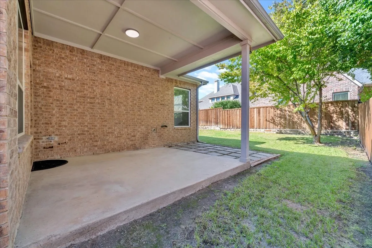 Covered concrete patio with a recessed light, brick exterior, and a manicured lawn