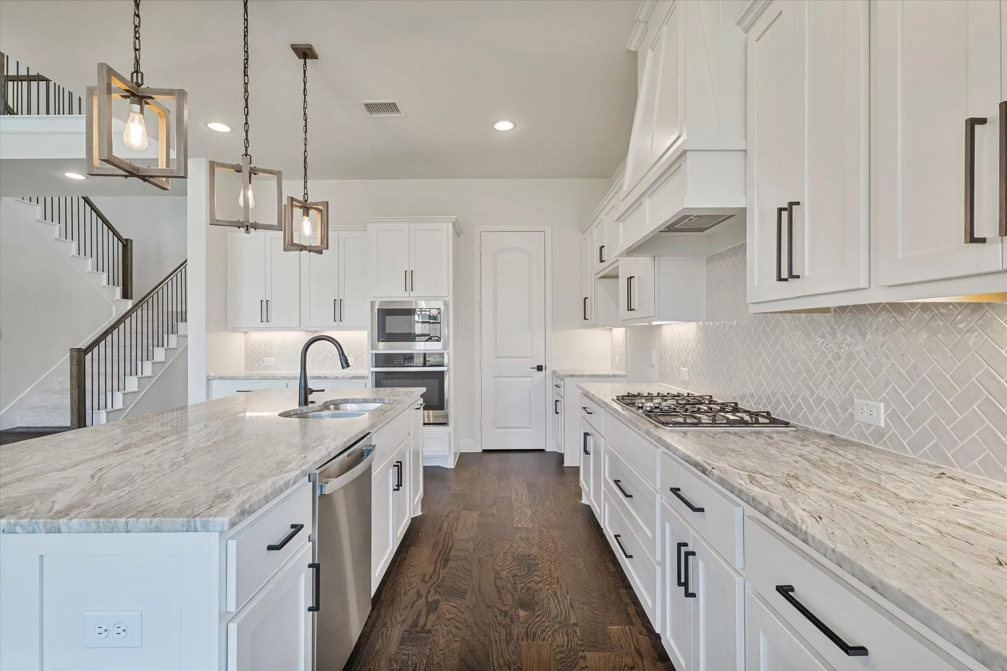 Kitchen featuring white shaker-style cabinetry, patterned stone countertops, a herringbone tile backsplash, stainless steel built-in appliances, and wood-finish flooring
