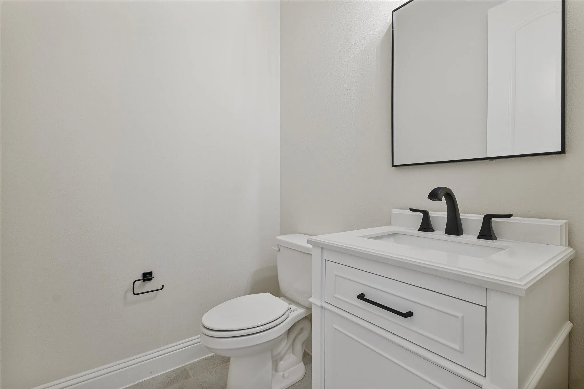 White vanity with a rectangular sink, matte black faucet, and matching cabinet hardware, complemented by a square mirror with a black frame