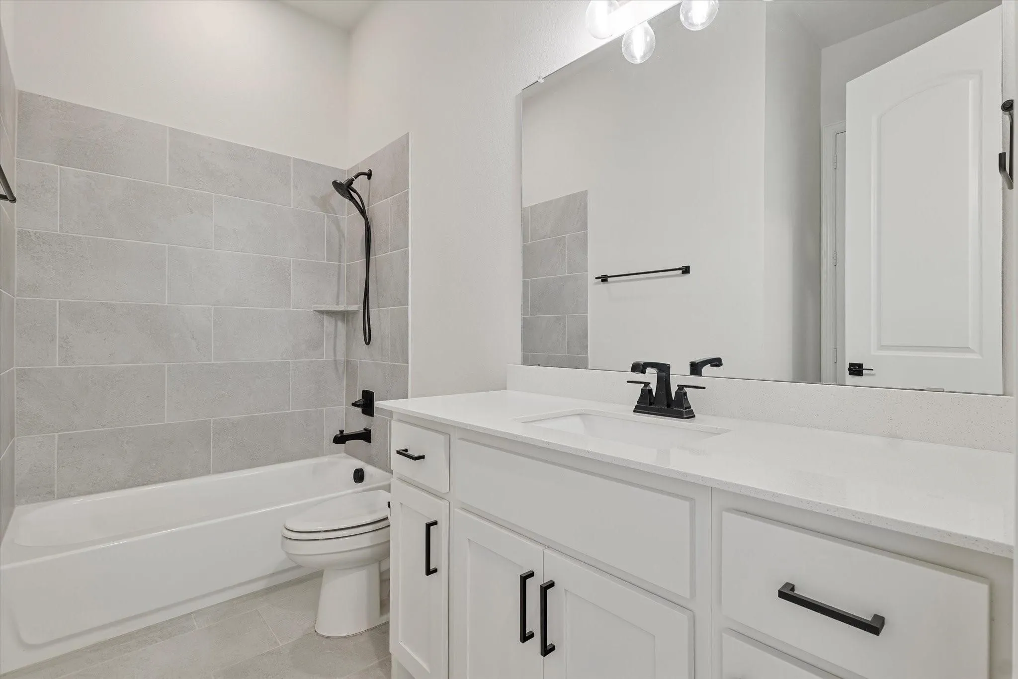 White vanity featuring a solid surface countertop, undermount sink, and matte black hardware, paired with a bathtub surround in grey rectangular tile and matte black plumbing fixtures