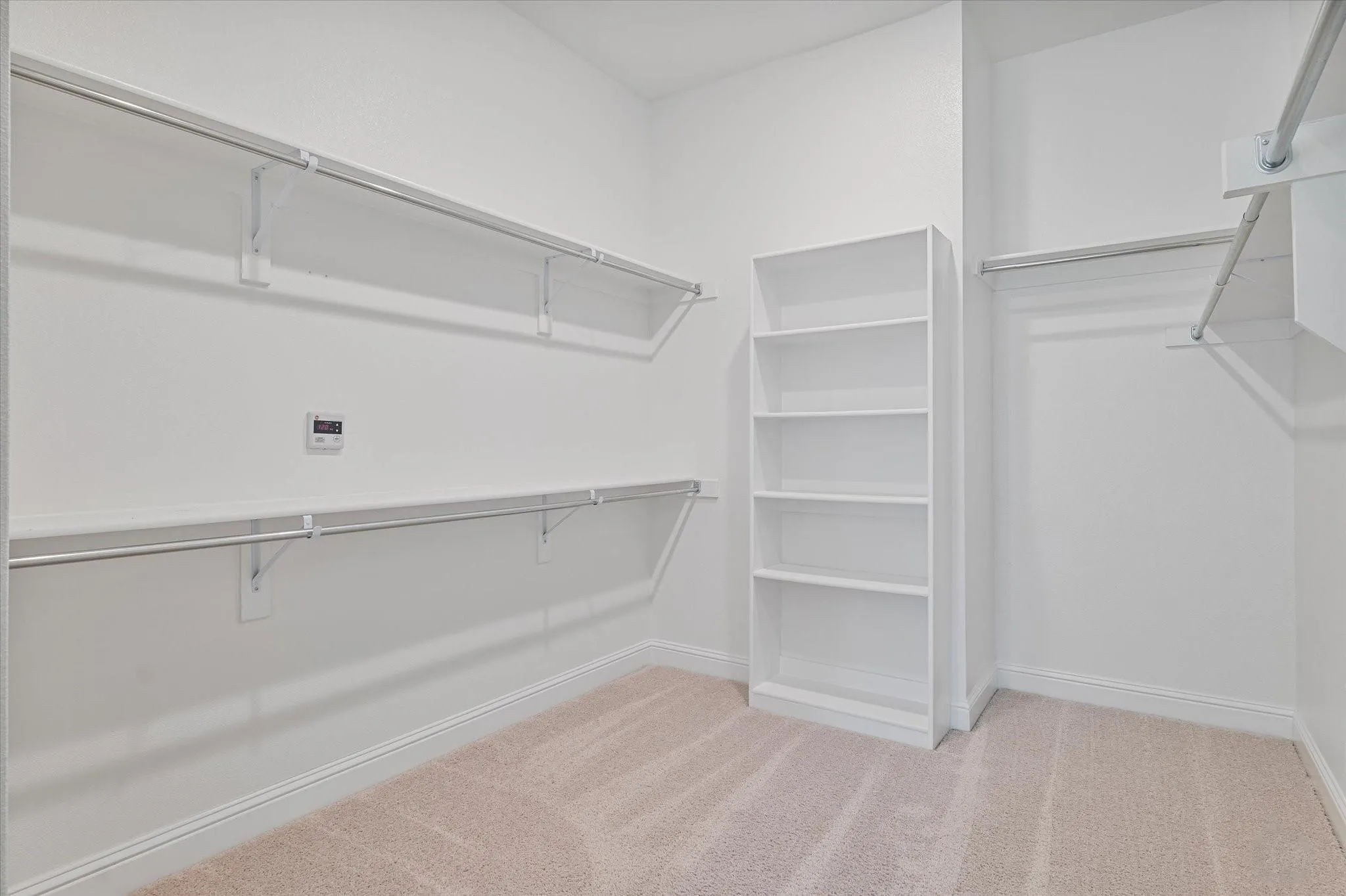 Walk-in storage area featuring wall-to-wall carpeting, stacked open shelving, and multi-tier metal clothing rods