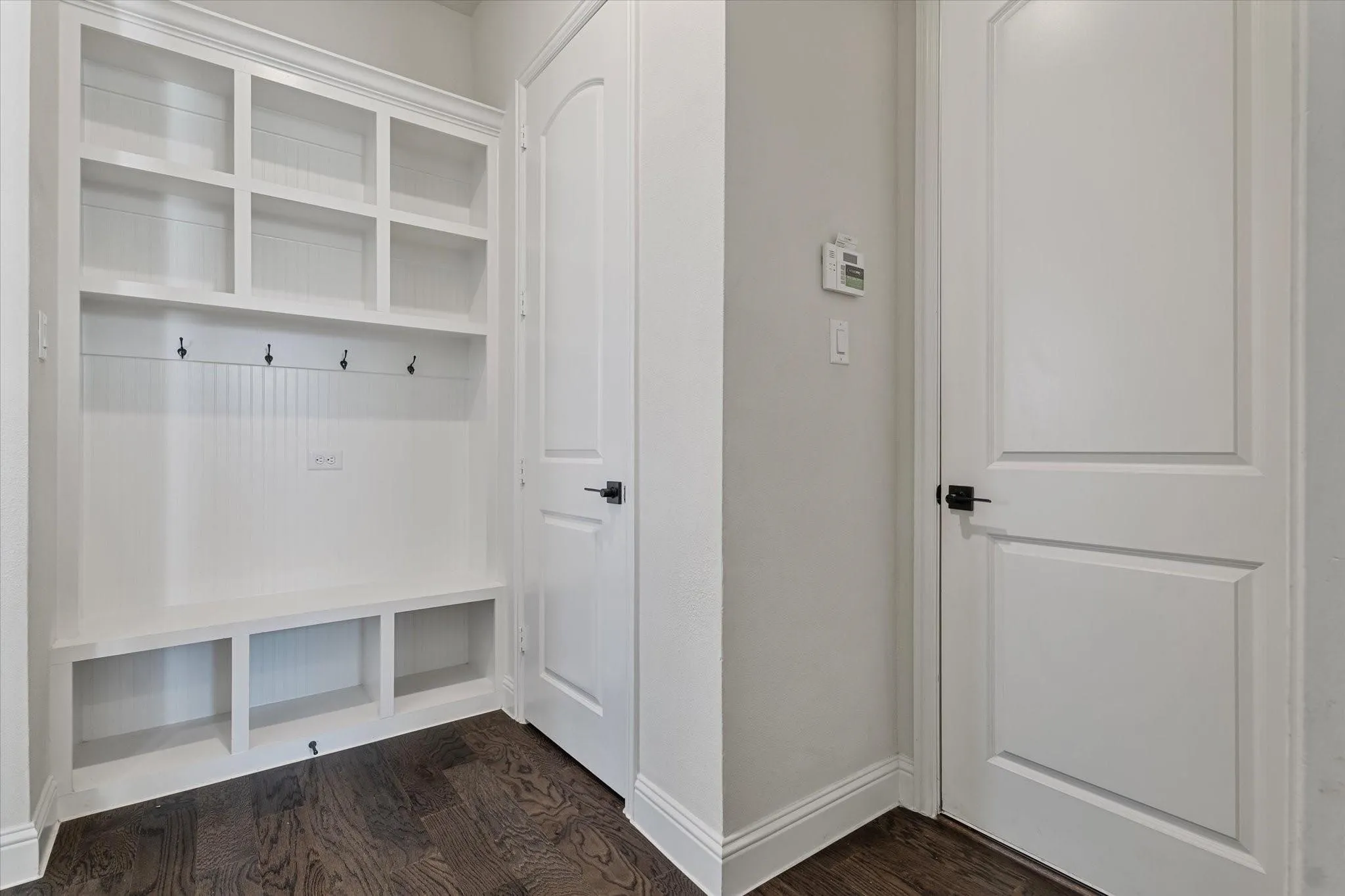 Built-in white storage cabinetry with beadboard paneling, integrated coat hooks, open shelving, and wood-finish flooring accented by arched-panel interior doors with matte black hardware