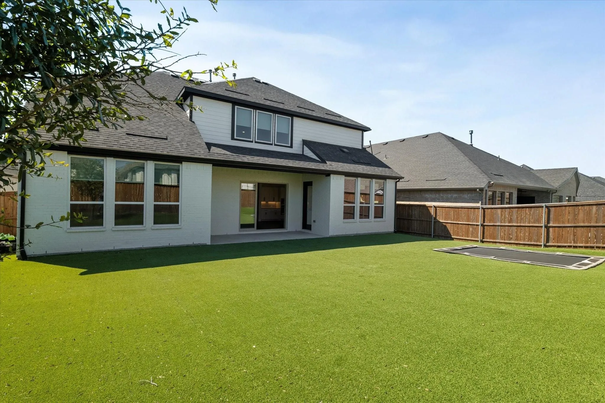 Rear exterior featuring a white brick and horizontal siding facade, multiple large windows, a paved patio, and a fully fenced private yard