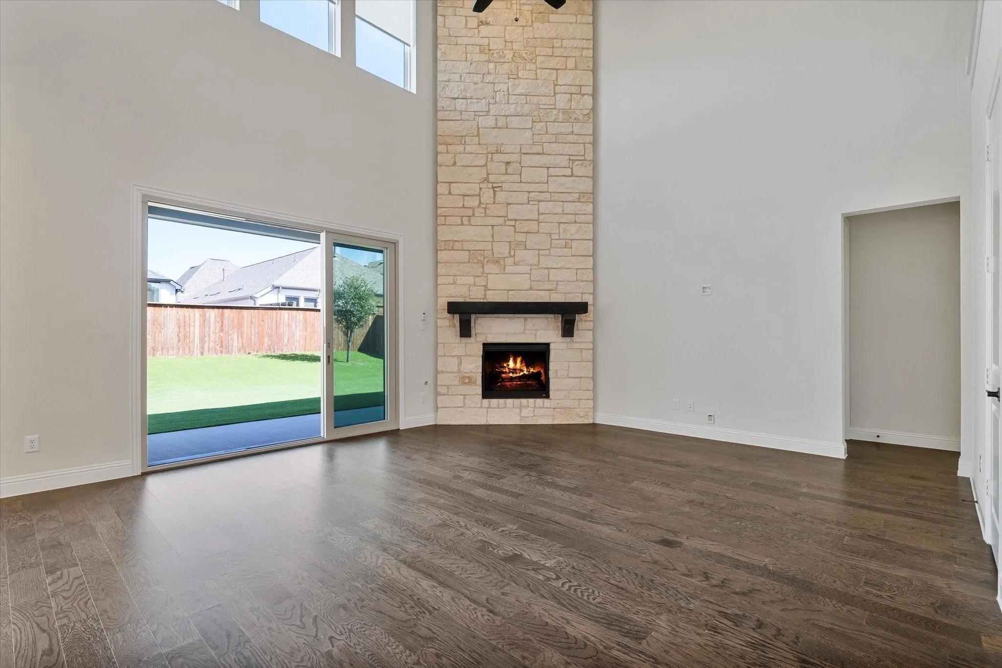Double-height living area featuring wood-finish flooring, floor-to-ceiling stone fireplace, dark wood mantel, and sliding glass doors