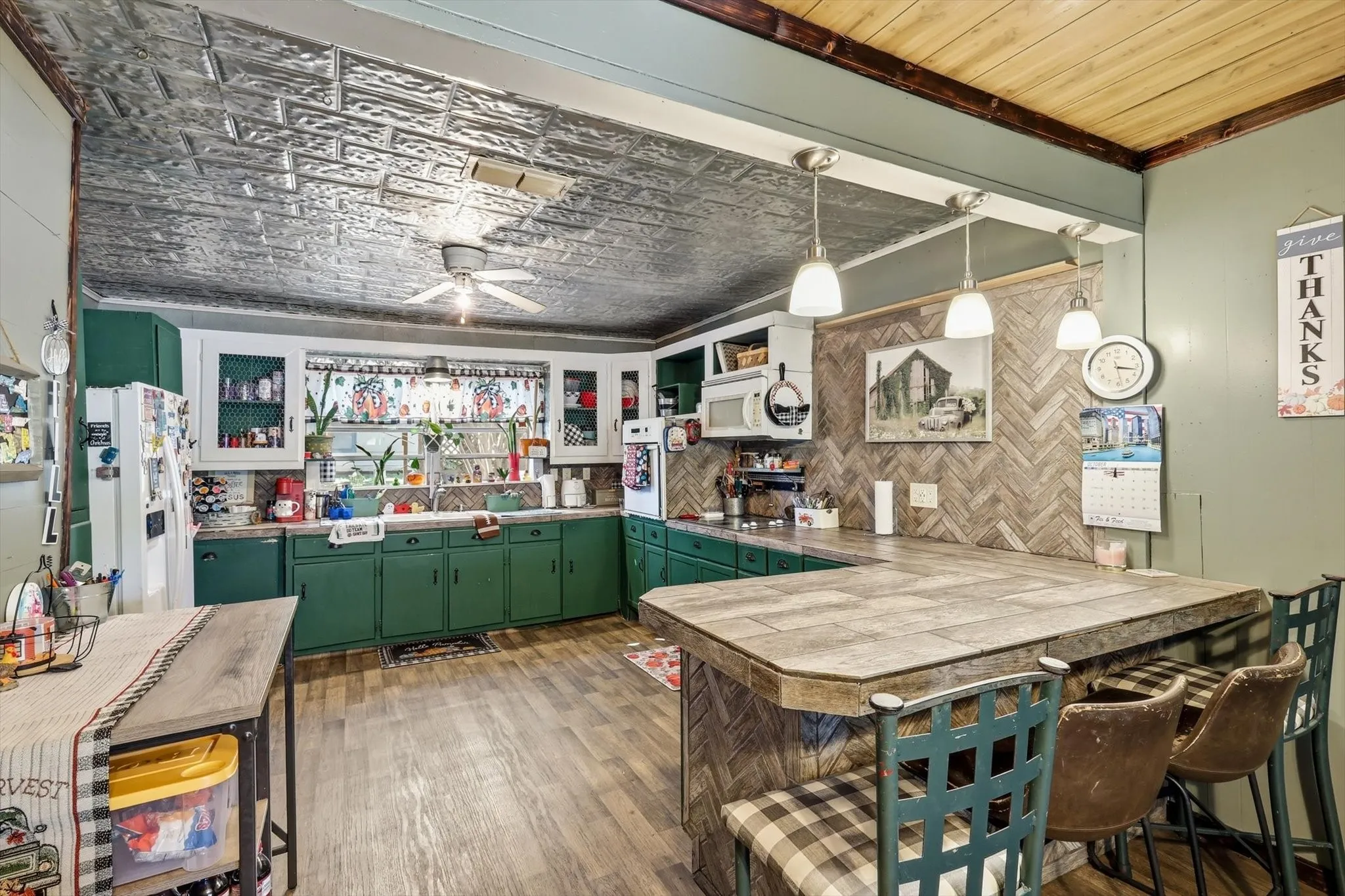Kitchen featuring a metallic-finish decorative ceiling, wood-finish flooring, herringbone-patterned tile backsplash, peninsula counter with built-in cabinetry, and pendant lighting