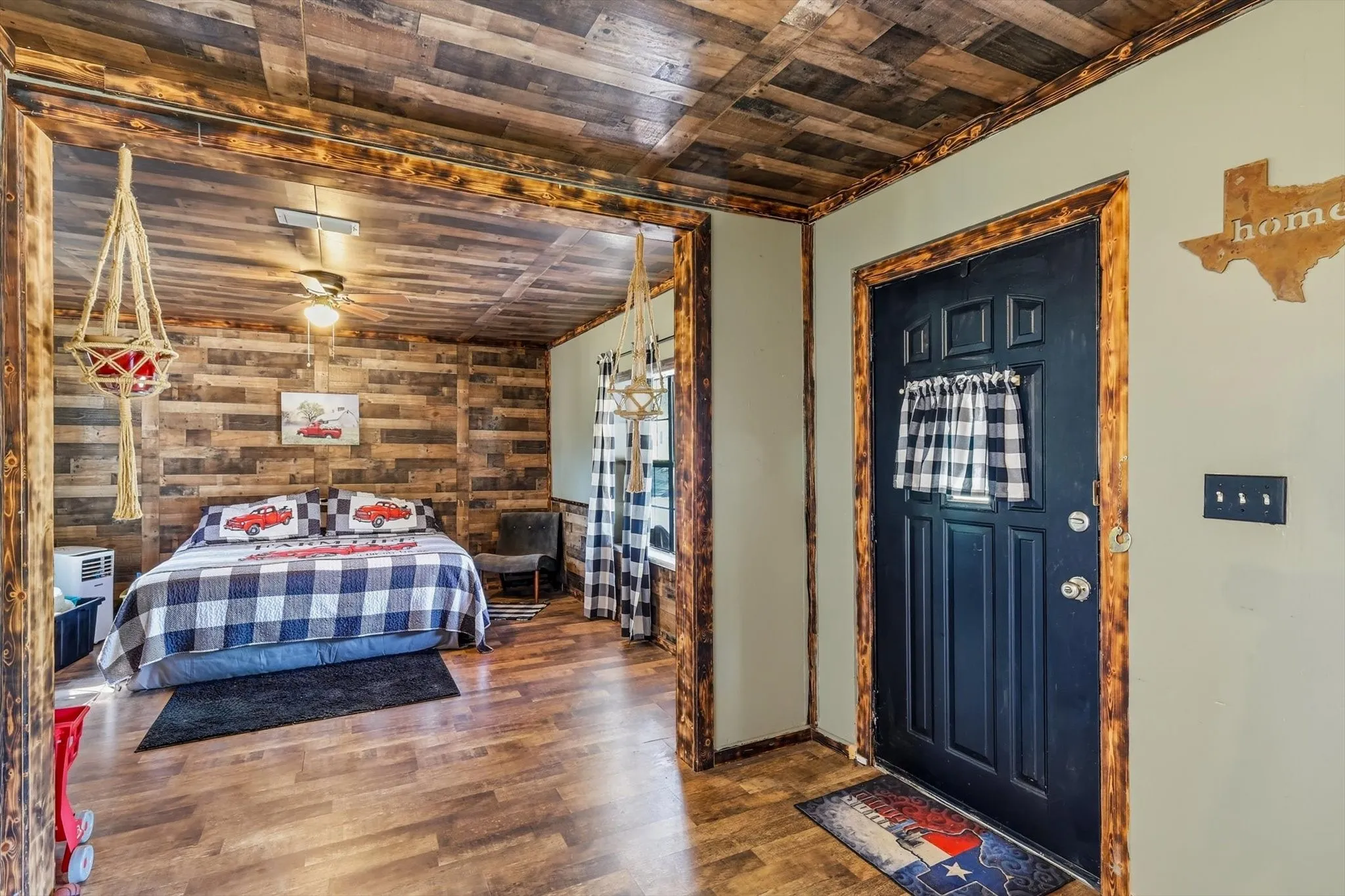 Interior featuring wood-plank wall and ceiling paneling, wood-finish flooring, custom wood door casing, and a black exterior-style entry door