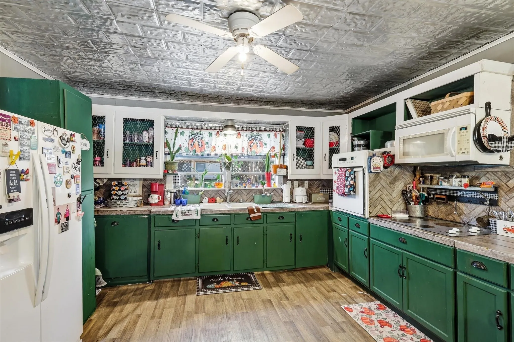 Kitchen featuring decorative pressed-tin ceiling, green cabinetry with glass-front uppers, herringbone-patterned tile backsplash, and wood-finish flooring